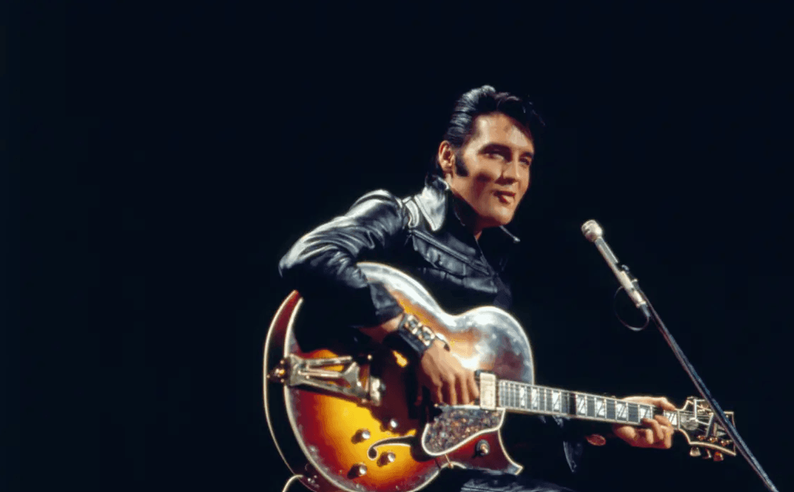 Elvis Presly Playing Guitar infront of a microphone with a black background